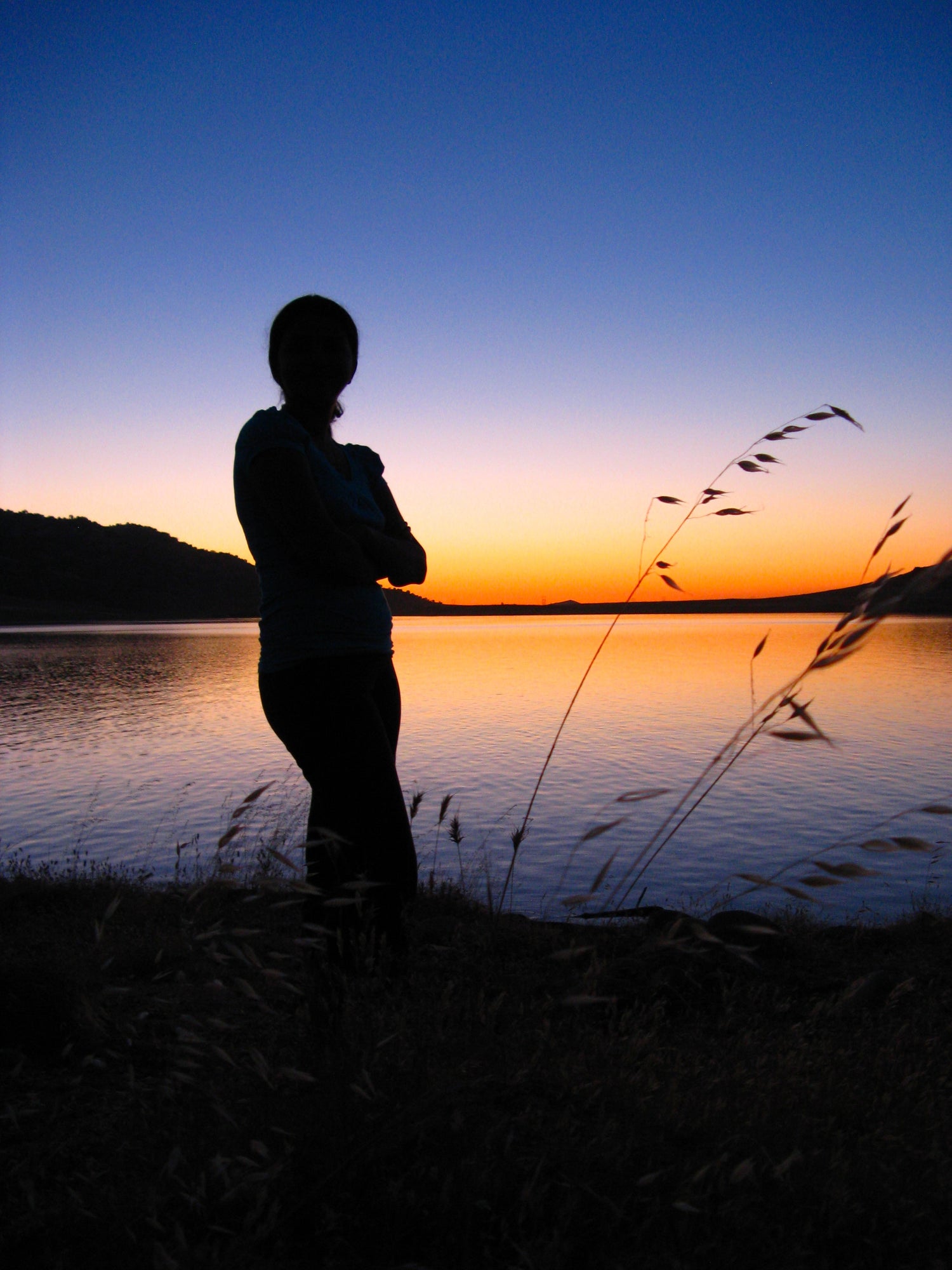 Silhouette of a person standing by a lake at sunset